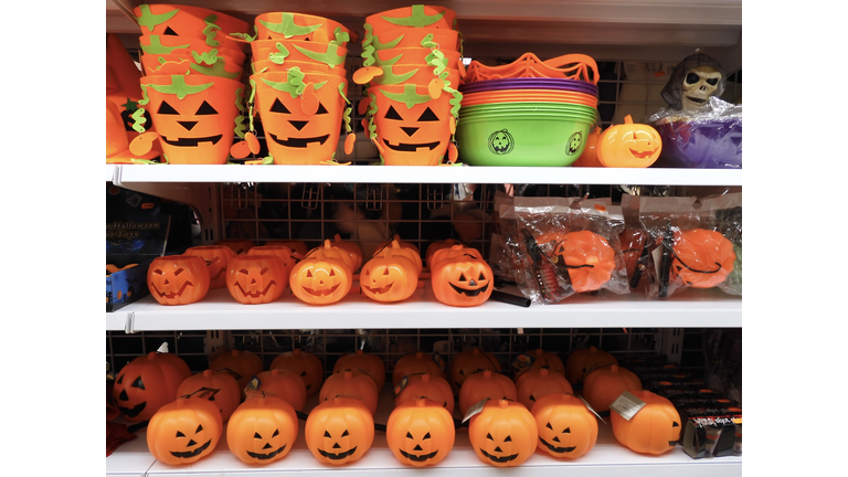 Plastic Halloween pumpkins and felt Halloween buckets on store shelves, along with other items such as a plastic skull or spider web.