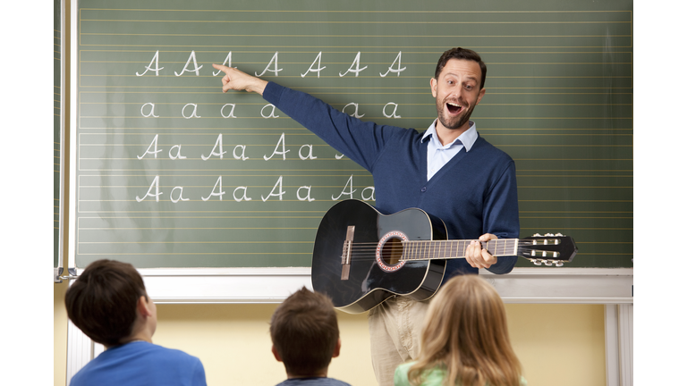 Teacher with guitar at blackboard showing variations of letter A