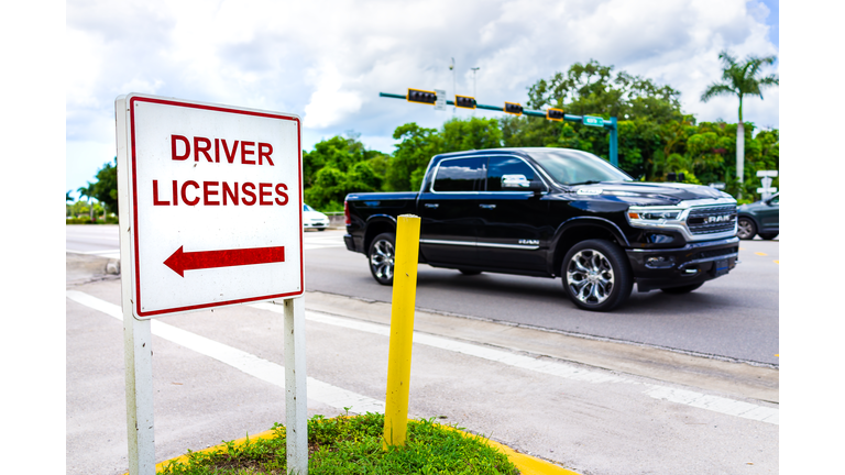 Downtown street road with car and roadside sign signpost for directions to driver license office for renewal