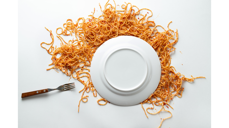A fallen white ceramic plate of spaghetti, with a fork beside it. Pasta bolognese in tomato sauce is scattered on a white background or table. The concept of vegetarian and vegan food. Food background. Copy of the text space.