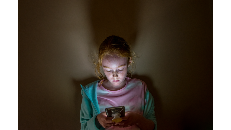 Young girl looking into mobile phone screen, in dark room