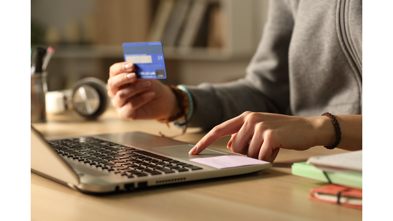Student hands paying with credit card on laptop at night