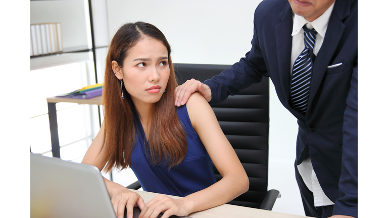 Angry unhappy Asian secretary woman looking hand's boss touching her shoulder in workplace. Sexual harassment in office