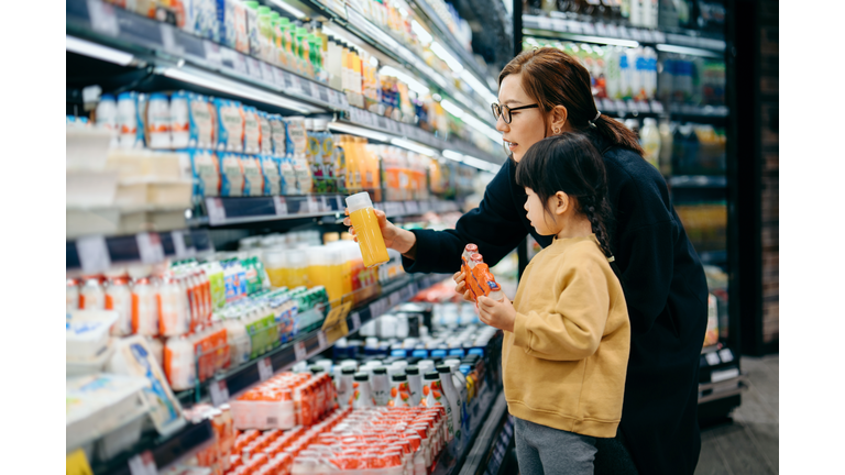 Young Asian mother and her little daughter grocery shopping in supermarket. they are choosing fresh fruit juice together along the beverage aisle. Routine grocery shopping. Healthy eating lifestyle