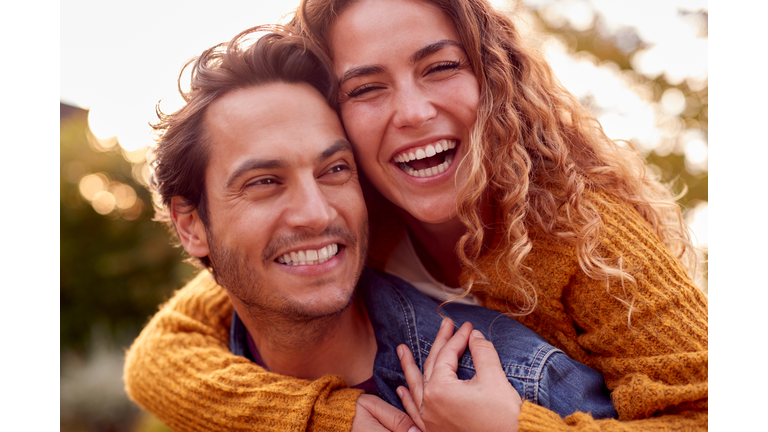 Portrait Of Happy Loving Couple With Man Giving Woman Piggyback As They Hug In Autumn Park Together