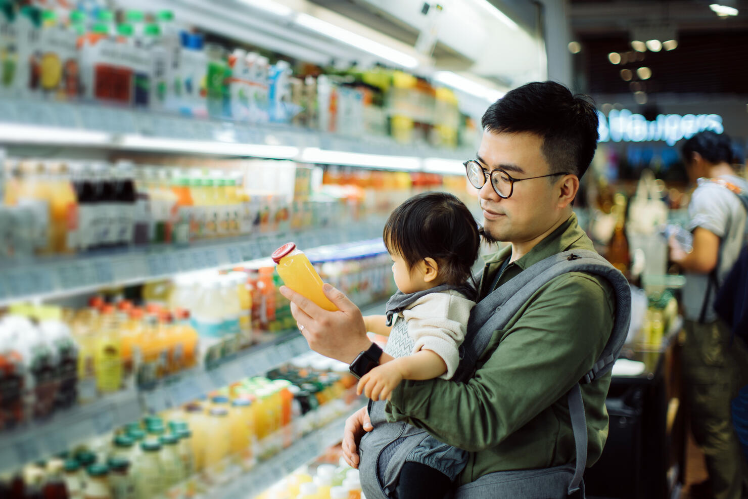 Young Asian father with cute little daughter grocery shopping for fresh fruit juice in supermarket