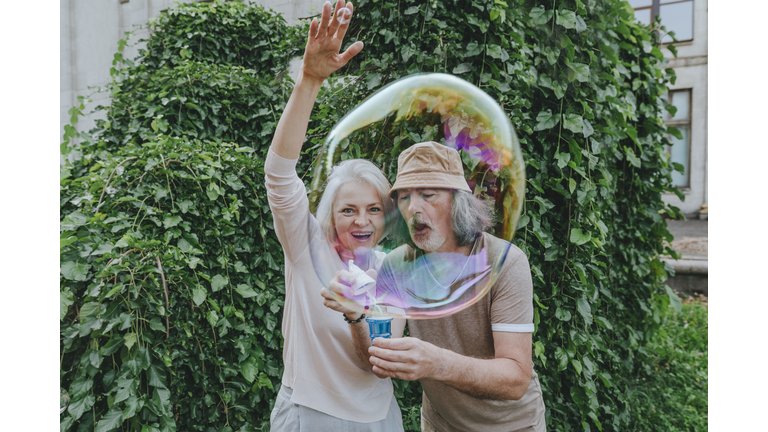 Happy mature woman enjoying by senior man making bubbles in park