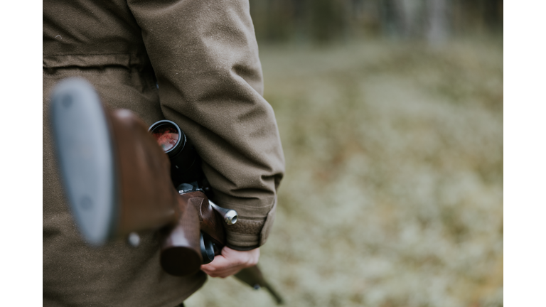 Close up shot of man with hunting rifle walking in the autumn forest