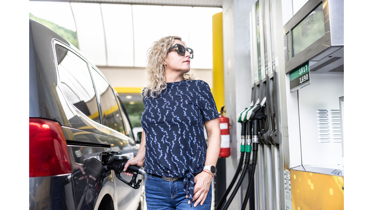 A female driver fills diesel fuel in her car and checks the amount filled at the gas station.