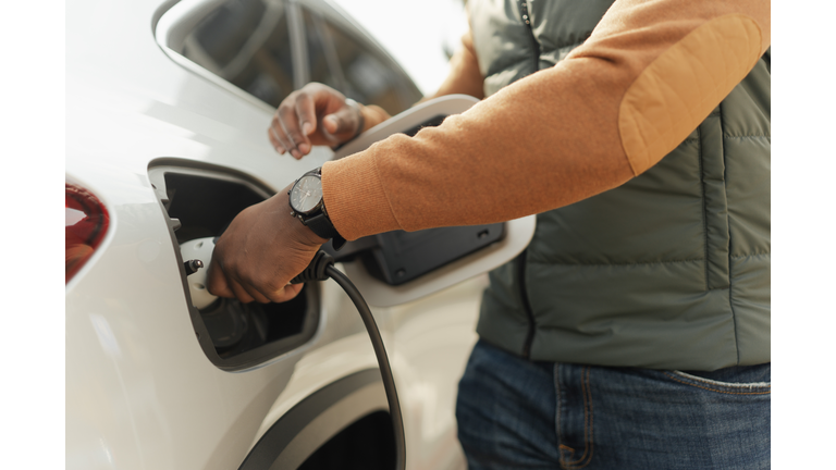 Close-up of young multiracial man charging electric car.