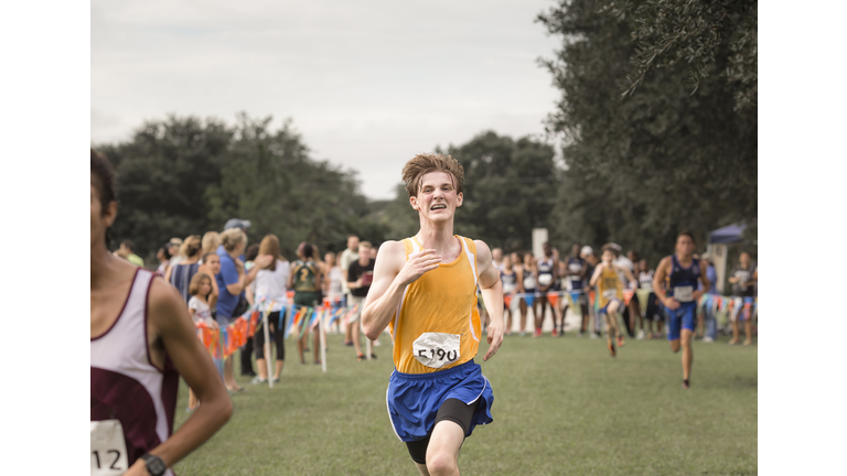 Teen male cross country runner with braces crosses finish line in race