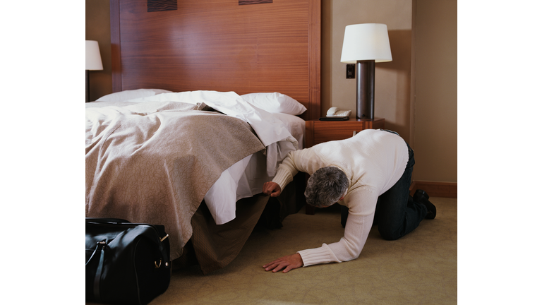 Man kneeling on floor in hotel room, looking under bed