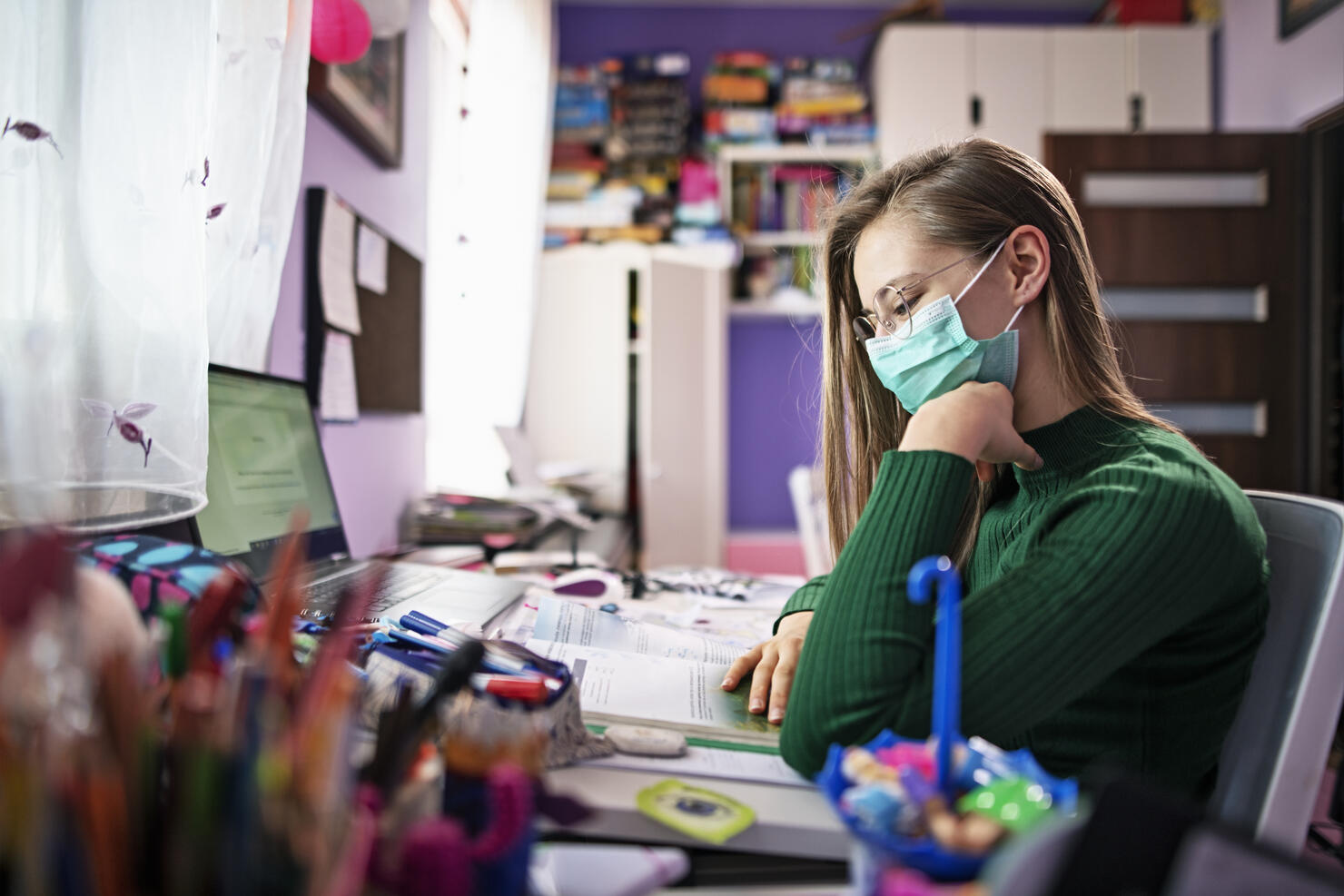 Teenage girl wearing surgical mask doing homework in her room.