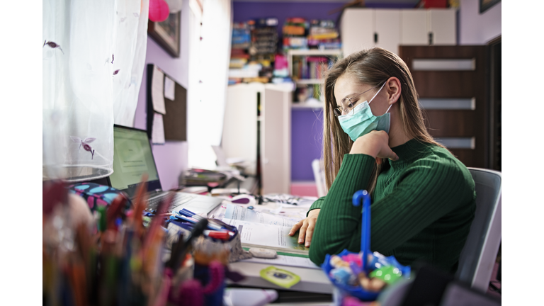 Teenage girl wearing surgical mask doing homework in her room.