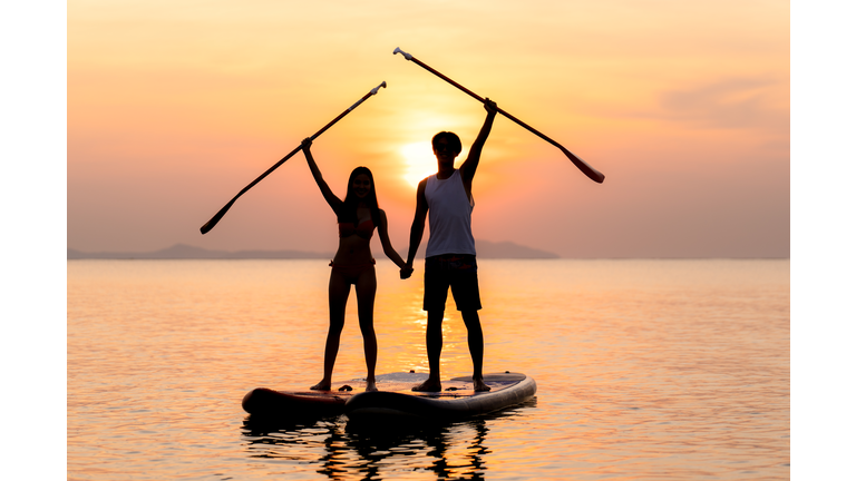 Stand up paddle board couple paddleboarding. Young Asian couple on summer vacation.