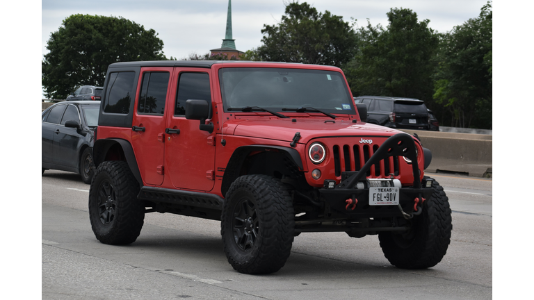 A portrait of a red Jeep Wrangler SUV traveling down a highway in moderate traffic