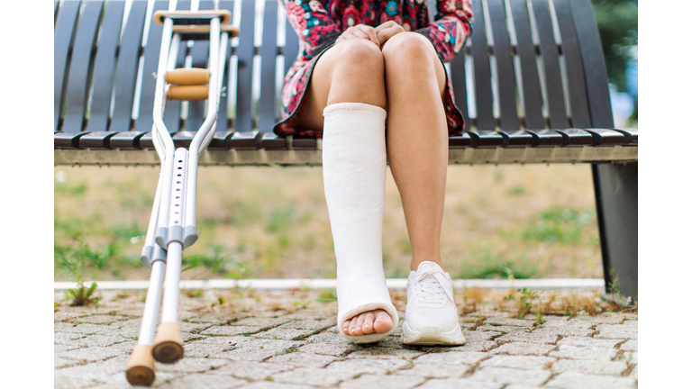 Young woman with a cast on her leg sitting on a bench