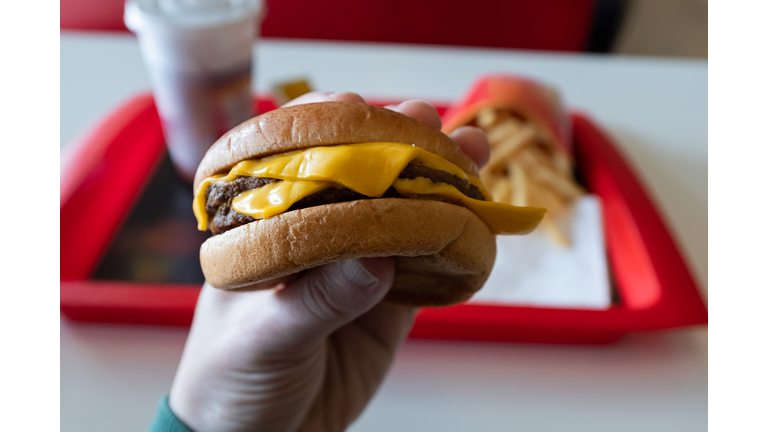 A young man is holding a piece of hamburger in his hands. A guy or a man eats fast food. A hungry skinny guy is eating an appetizing burger. The concept of unhealthy food, diet, overeating, gluttony, dependence on food. Fast food restaurant, snack bar.
