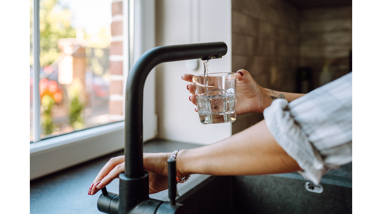 Water filtration in domestic kitchen. Unrecognizable woman hands pouring water in drinking glass from tap