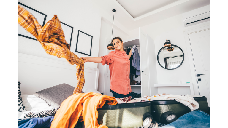 Happy woman packing suitcase in bedroom.