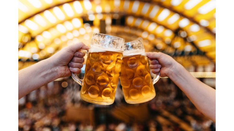 two hands clinking beer glasses in octoberfest marquee