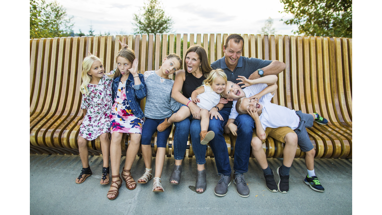 Silly and funny family portrait on wooden bench outside.