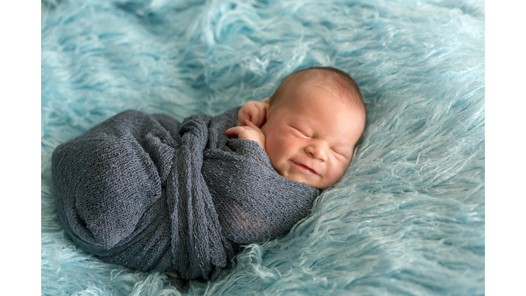 Happy smiling newborn baby in wrap, sleeping happily in cozy blue fur, cute infant baby