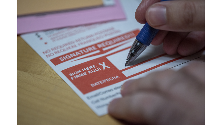 Absentee ballot form with man's hand using pen sign at bottom red box