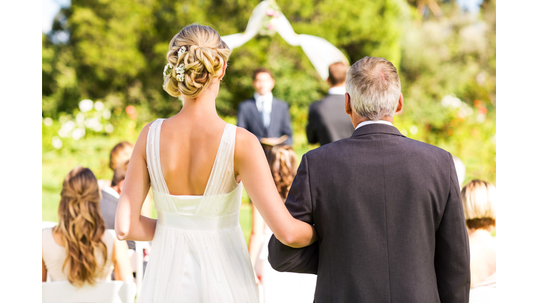 Bride And Father Walking Down The Aisle During Outdoor Wedding