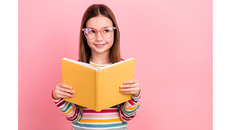 Photo of thoughtful little young schoolgirl kid reading favorite novel literature minded look empty space isolated on pink color background