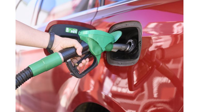 Close-up of a woman standing at a gas station filling her car with gasoline.