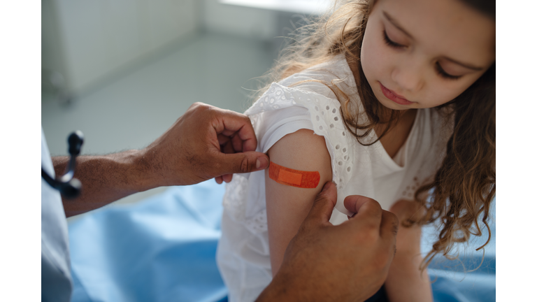 Young doctor giving plaster strip to little girl after vaccination.