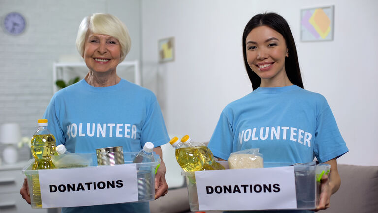 Smiling senior and young volunteers holding food donation boxes looking camera