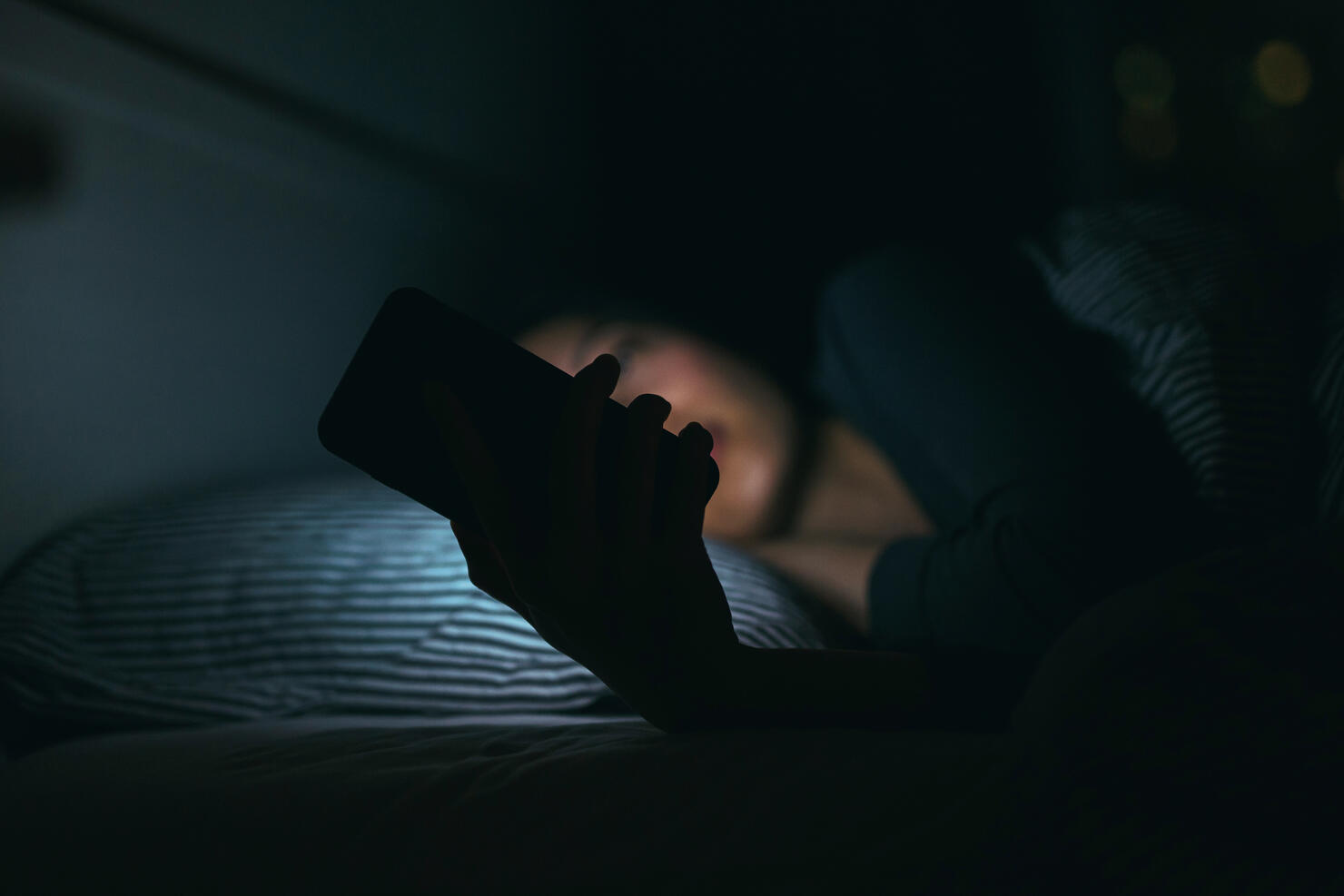 Young woman text messaging on smartphone while relaxing and lying on bed at night