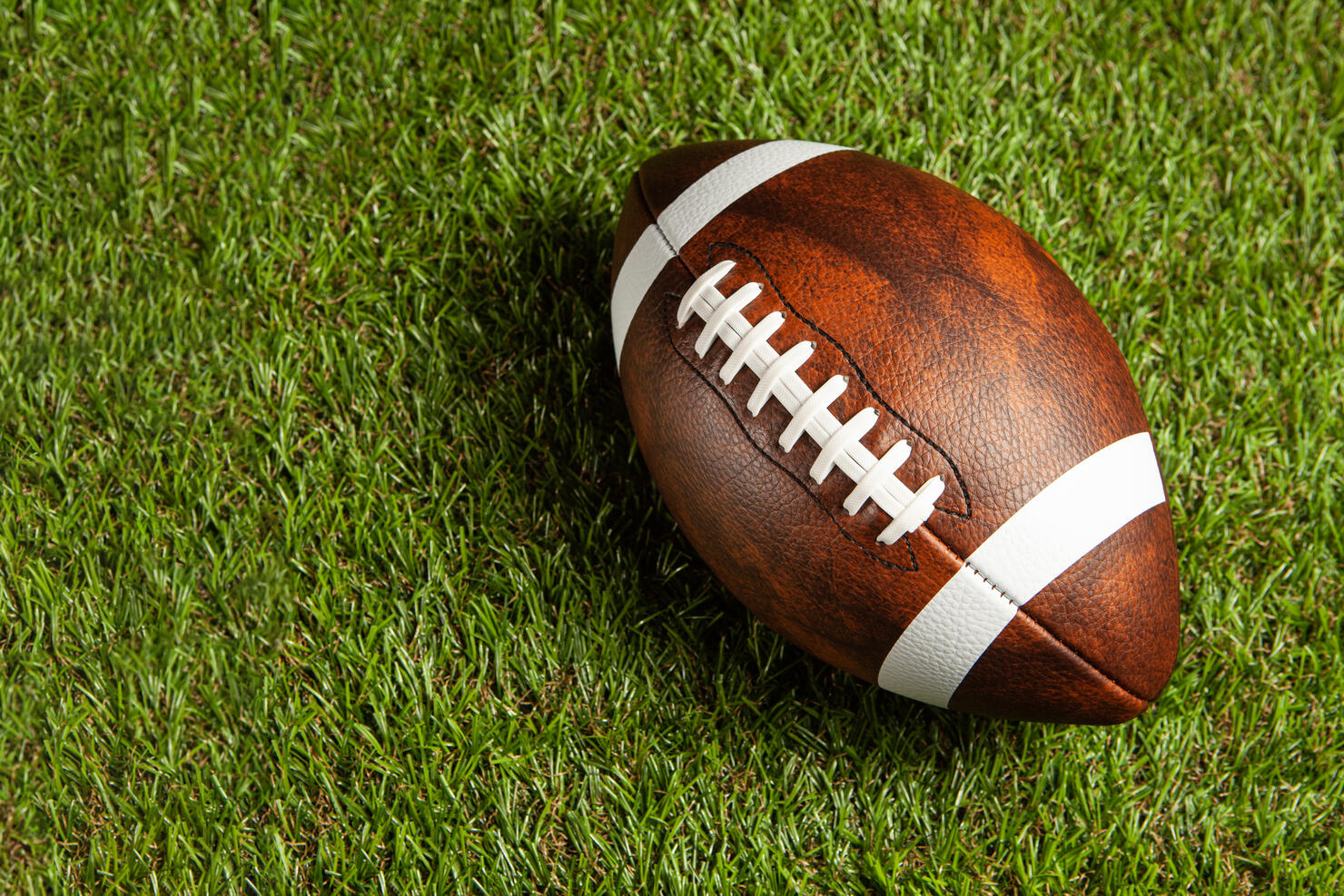 American football ball on green grass field background.