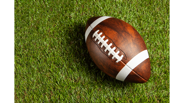 American football ball on green grass field background.