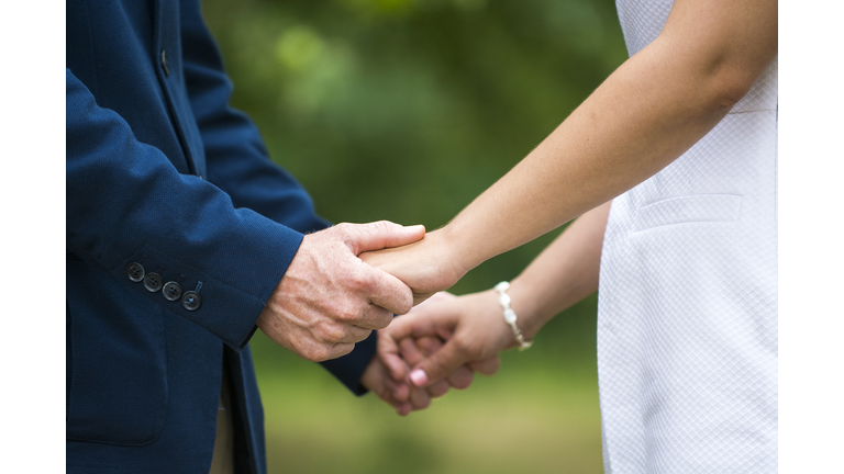 Midsection Of Bride And Groom Holding Hands While Standing Outdoors