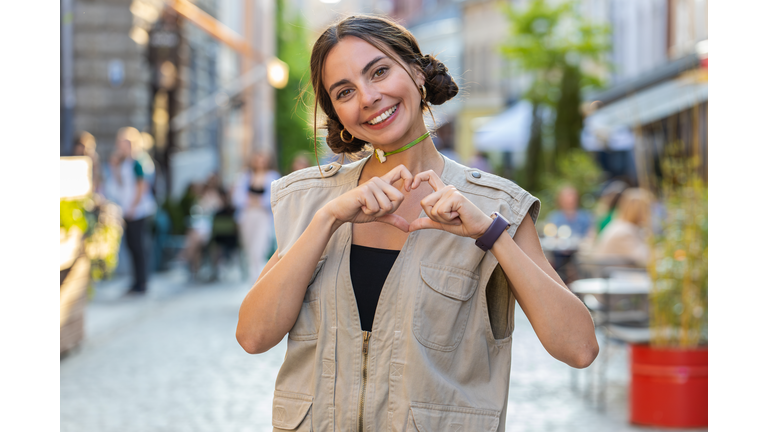 Young woman makes symbol of love, showing heart sign to camera, express romantic positive feelings