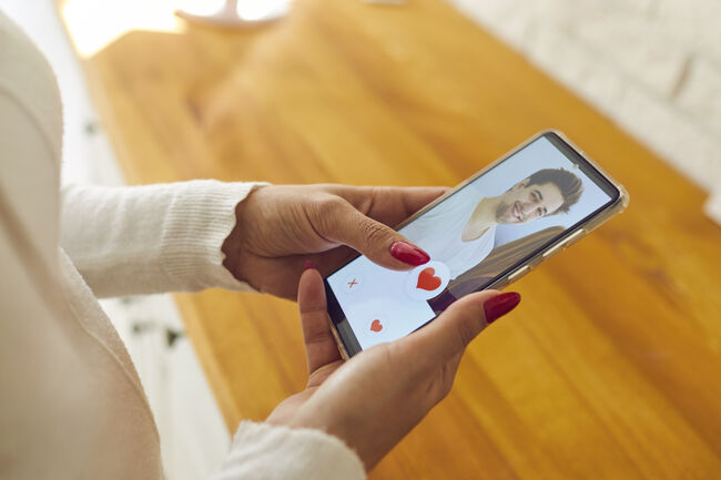 Single woman holding mobile and giving like to man's profile picture on dating app