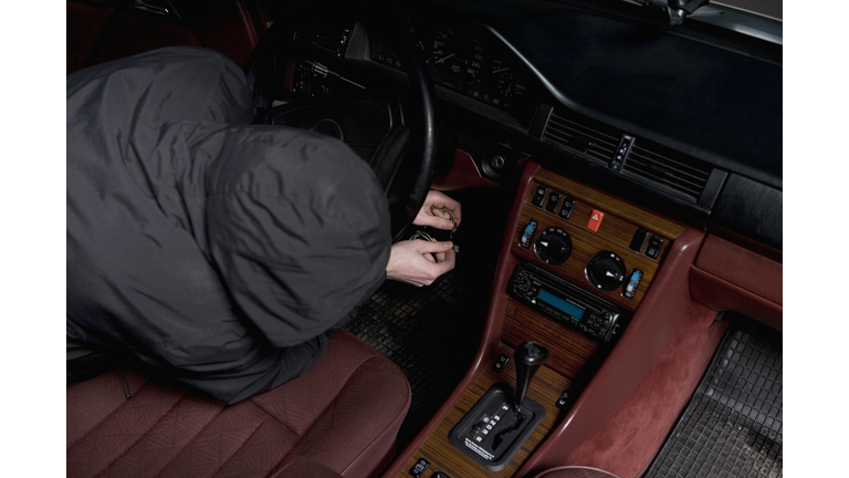 A hooded man starting a car with ignition circuit wires