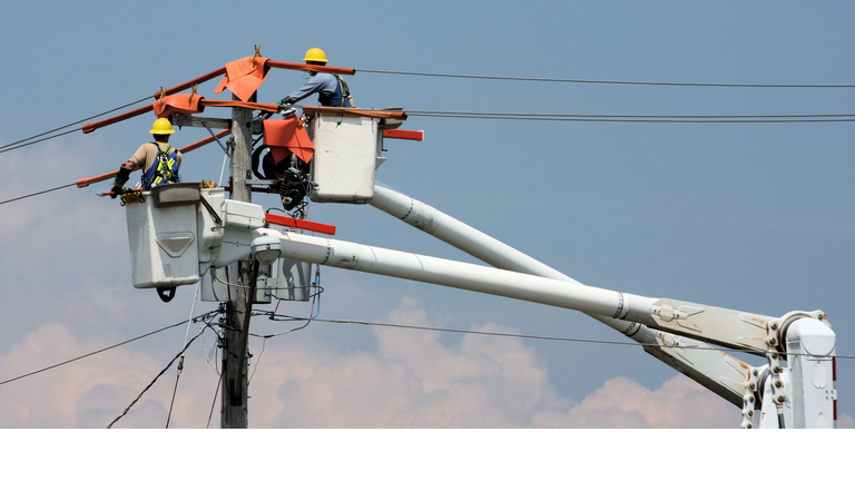 Two workers in a crane repairing a power pole