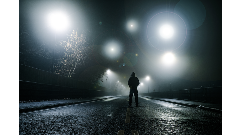 A fantasy, sci fi concept. Of a man standing in the middle of a road with mysterious UFO lights floating above him. On a spooky foggy winters night.