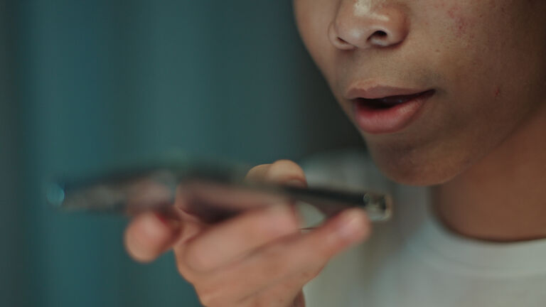 Teenager student talking with a voice assistant on smartphone at night.