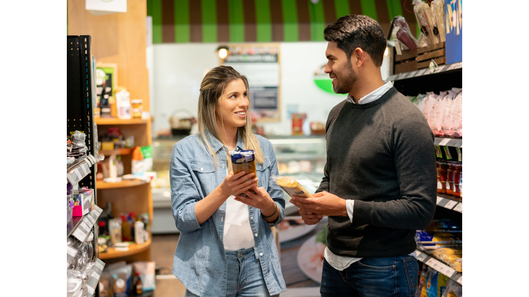 Happy couple at the supermarket looking at each other talking while holding a package of pasta