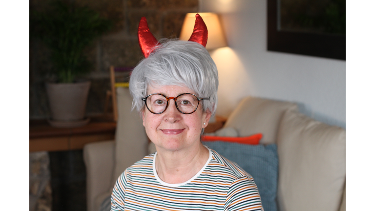 Senior woman with devil horns at home