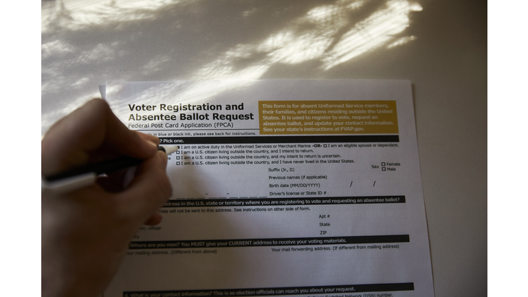 Overhead shot of a person filling out a voter registration and absentee ballot forum at home.