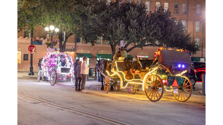 people enjoy to have a ride by night in the horse drawn carriage with colorful neon light in San Antonio at the river walk area