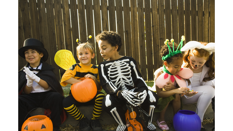 Children in Halloween costumes sitting on sidewalk