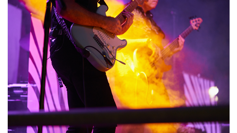 Midsection of performance musician playing guitar in rock music concert