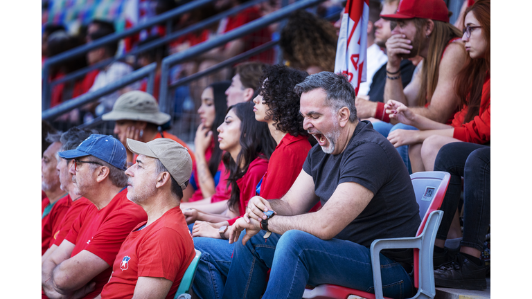 Older adult male in crowd of fans yawns and checks the time on his watch during big soccer match